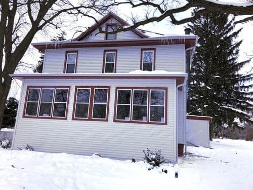 A house with new light gray siding and red trim in the snow.