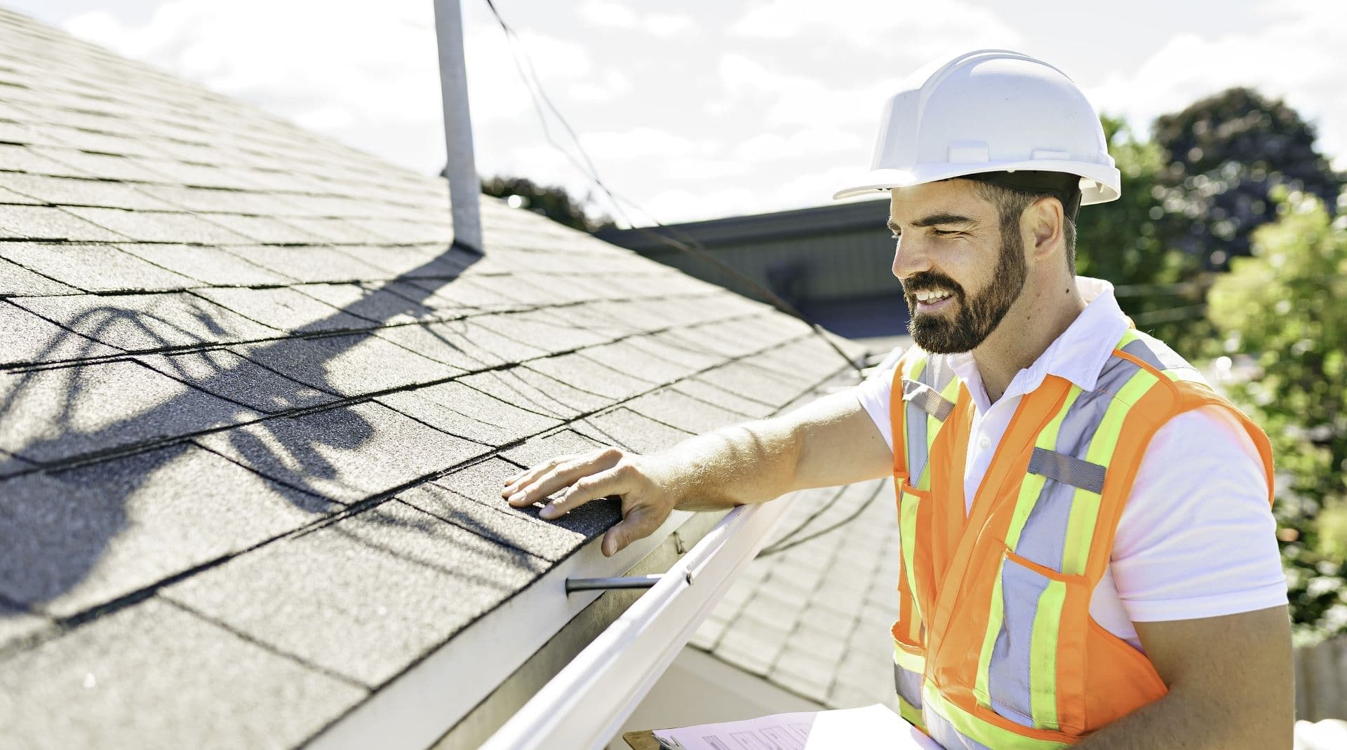 A worker in a safety vest and helmet inspects a roof.