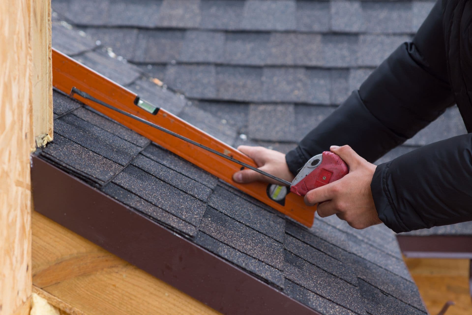 A worker measures and installs new roofing shingles.